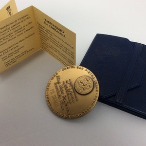 K&ouml;nnte beinhalten: Eine goldfarbene Medaille mit der Inschrift "Alma Mater Studiorum Secularia Nona" und dem Text "CM PIL THOMAS" auf der Vorderseite. Die R&uuml;ckseite der Medaille zeigt ein Wappen mit dem Text "CASTEL SAN PIETRO TERME - 1338 - 1988" und dem Text "UNIVERSITA' DEGLI STUDI DI BOLOGNA" in einem Kreis um das Wappen.