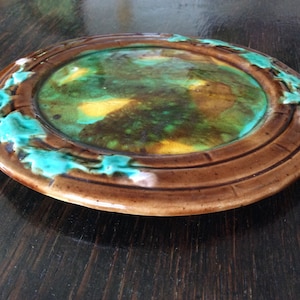 May include: A brown ceramic plate with a green and yellow glaze. The plate has a raised rim with a decorative design.