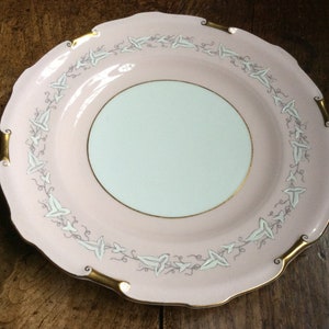 Puede incluir: Un plato de porcelana rosa y blanco con un borde dorado y un delicado diseño floral. El plato tiene un borde festoneado y es perfecto para servir una variedad de platos.