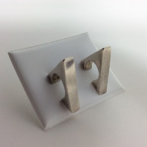 May include: A pair of silver geometric earrings with a triangular shape. The earrings are simple and modern in design.