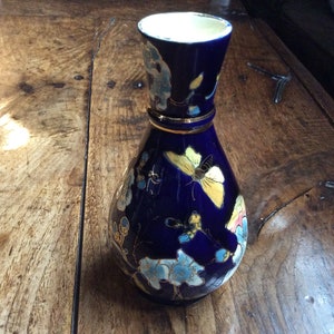 May include: A cobalt blue ceramic vase with a gold rim and floral and butterfly designs in yellow, white, and blue.