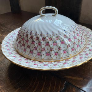 May include: A white porcelain butter dish with a lid. The dish features a floral pattern with pink, red, and blue flowers. The lid has a gold trim.