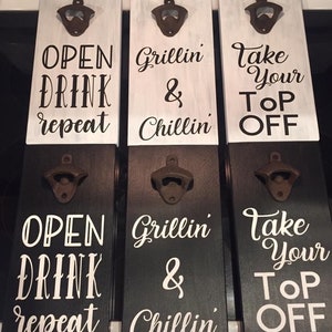 May include: Three wooden bottle openers with black and white painted signs. The signs read "Open Drink Repeat", "Grillin' & Chillin'" and "Take Your Top Off".