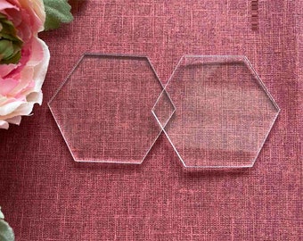 May include: Two clear acrylic hexagonal coasters on a red textured surface.