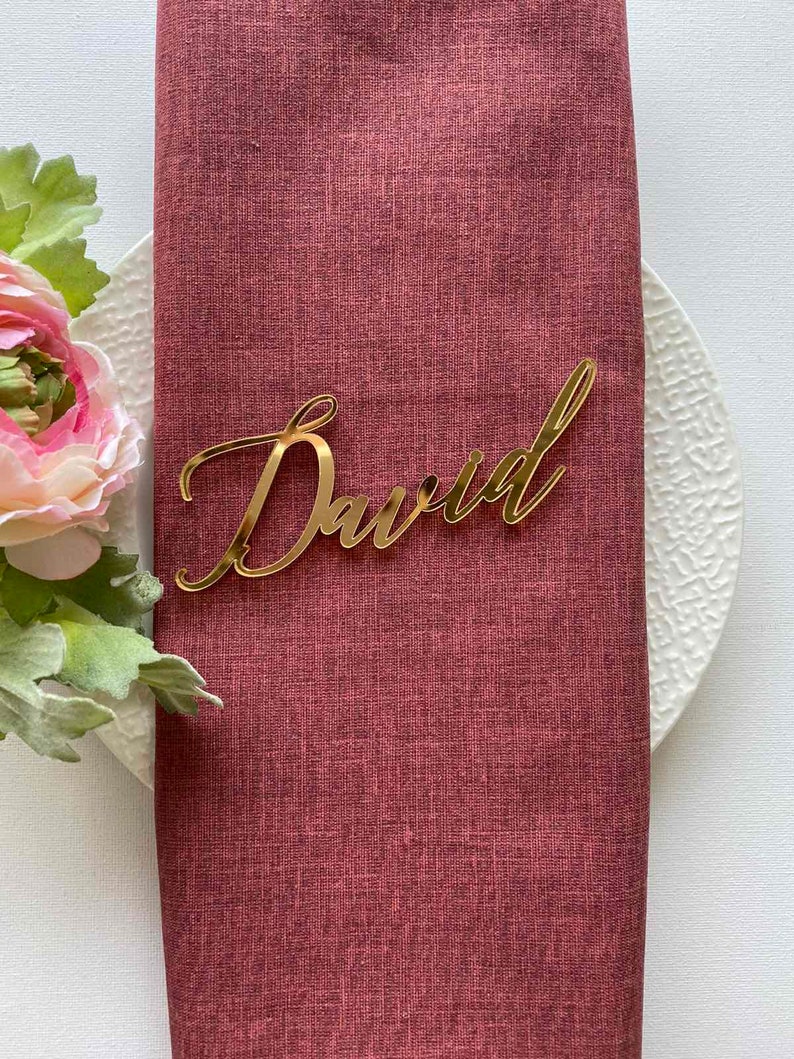 Puede incluir: Tarjeta de lugar de acr&iacute;lico dorado con el nombre "David" escrito en cursiva.