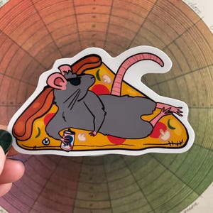 May include: A cartoon rat wearing sunglasses and a baseball cap is lying on a slice of pizza with a can of soda. The rat is wearing a grey shirt and has a pink tail.
