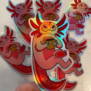 Peut inclure: Plusieurs autocollants holographiques représentant un axolotl de dessin animé tenant une tasse. Les axolotls sont roses avec des branchies rouges et une tête jaune-orange. Les autocollants ont une finition brillante et irisée.
