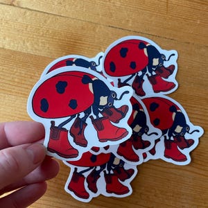 May include: A stack of five ladybug stickers with red bodies, black spots, and black legs wearing red rain boots.