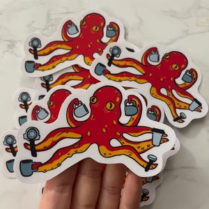 May include: A stack of red octopus stickers with yellow accents. Each octopus is holding a coffee cup and a coffee maker. The stickers are on a white surface.