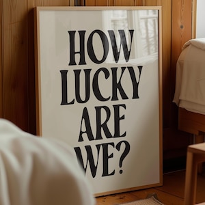 May include: A framed print with the text "HOW LUCKY ARE WE?" in black bold letters on a cream background.