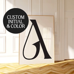 Puede incluir: Un póster en blanco y negro con una gran letra "A" estilizada en una fuente moderna. El póster está enmarcado en un marco de madera delgado y está colgado en una pared blanca en una habitación con suelo de madera.