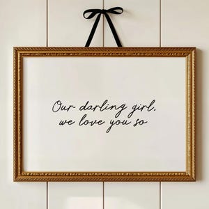 Peut inclure: Impression encadrée rectangulaire avec le texte "Our darling girl, we love you so" en écriture noire. Le cadre doré est orné de détails et un ruban noir est utilisé pour l'accrocher.