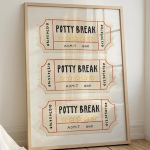 May include: A framed artwork featuring three "Potty Break" tickets. Each ticket has the text "Potty Break", four stars, and "Admit One". The tickets are in a light beige color with red and yellow accents, and a wooden frame.