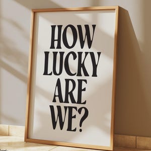 May include: A framed print with the text "HOW LUCKY ARE WE?" in bold, black letters on a white background.