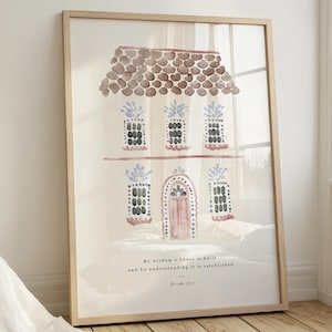Pode incluir: Impressão artística emoldurada de uma casa em aquarela. O telhado é marrom, as janelas são azuis e pretas e a porta é rosa. O texto na parte inferior diz: "Com a sabedoria se edifica a casa, e com a inteligência se estabelece."