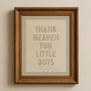 May include: A framed print with the text "THANK HEAVEN FOR LITTLE BOYS" in gray letters. The print has a light beige background with a striped border and is encased in a brown wooden frame.