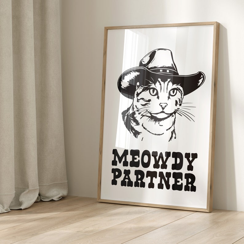 Pu&ograve; includere: Illustrazione in bianco e nero di un gatto con un cappello da cowboy con il testo "MEOWDY PARTNER".