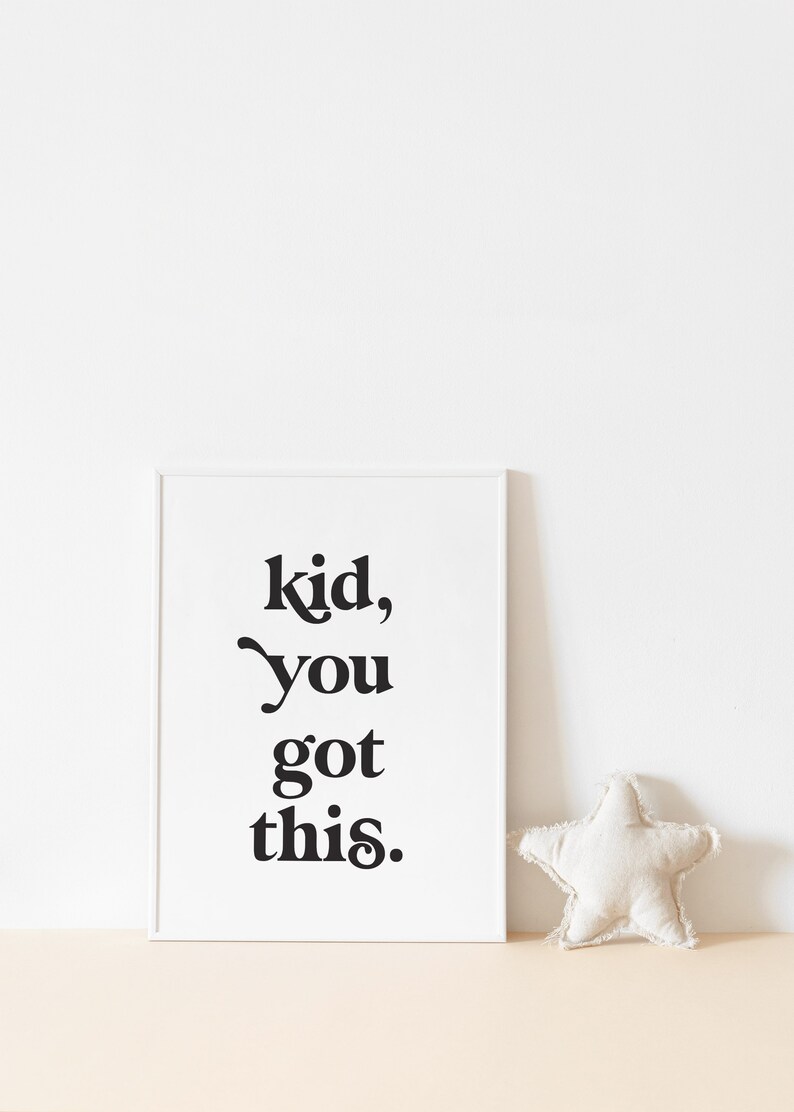 May include: A white framed print with black text that reads "kid, you got this." The print is on a light brown surface with a white star-shaped pillow.