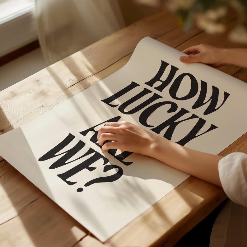 May include: A white poster with black text that reads "How lucky are we?" The poster is being held by a person's hand.