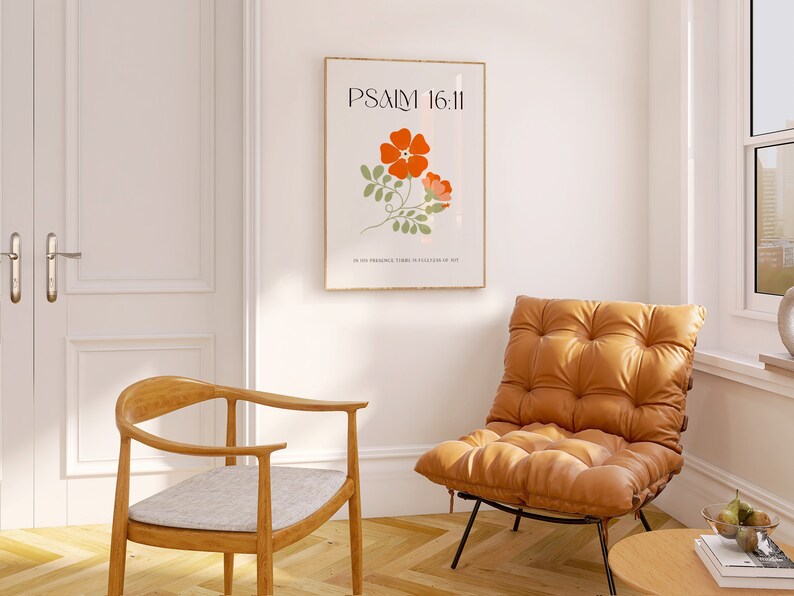 K&ouml;nnte beinhalten: Ein gerahmter Kunstdruck mit dem Text "PSALM 16:11" und einer floralen Illustration in Orange und Gr&uuml;n. Der Druck h&auml;ngt an einer wei&szlig;en Wand &uuml;ber einem braunen Ledersessel und einem Holzstuhl mit einem grauen Kissen. Vor dem Stuhl steht ein kleiner Holztisch.
