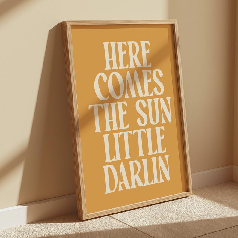 K&ouml;nnte beinhalten: Ein gerahmter Druck mit gelbem Hintergrund und wei&szlig;em Text, der "Here comes the sun little darlin" lautet.