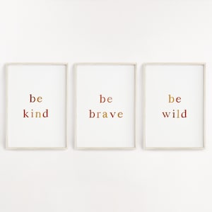 May include: Three framed prints with the words "be kind", "be brave", and "be wild" in a gradient of brown, orange, and yellow.