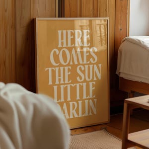 K&ouml;nnte beinhalten: Ein gerahmter Druck mit gelbem Hintergrund und wei&szlig;em Text, der "Here comes the sun little darlin" lautet.