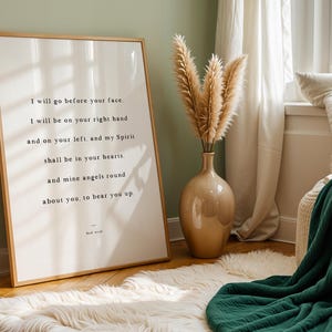 K&ouml;nnte beinhalten: Ein gerahmter Druck mit hellem Holzrahmen zeigt inspirierenden Text in schwarzer Schrift. Eine beige Vase enth&auml;lt getrocknetes Pampasgras. Eine gr&uuml;ne Decke und ein wei&szlig;er Kunstfellteppich verleihen dem Raum Textur. Der Text lautet: "I will go before your face..."