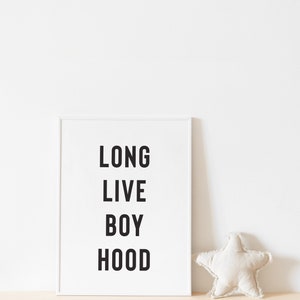 May include: White framed print with the text "LONG LIVE BOY HOOD" in black lettering. A white star-shaped pillow is on a light brown surface.