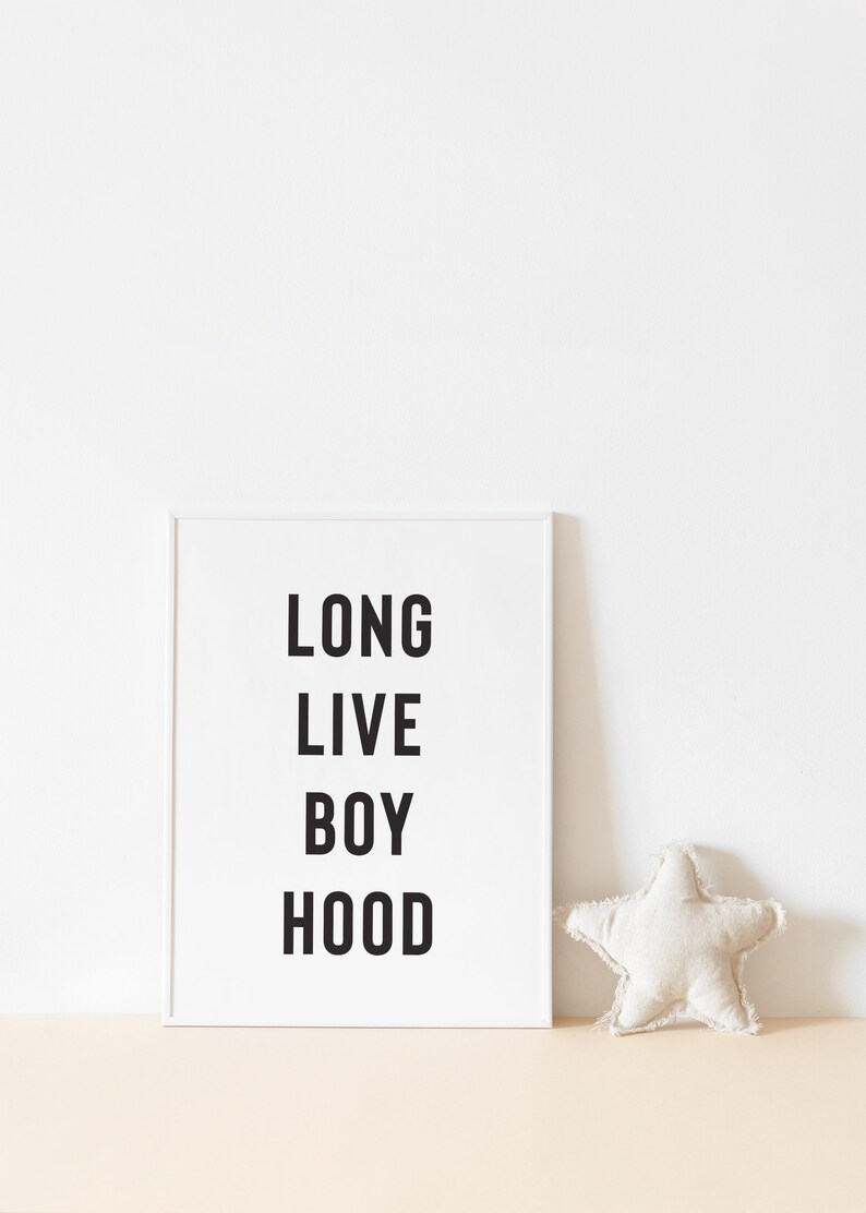 May include: White framed print with the text "LONG LIVE BOY HOOD" in black lettering. A white star-shaped pillow is on a light brown surface.