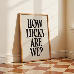 May include: A framed print with the text "HOW LUCKY ARE WE?" in black bold letters on a cream background.