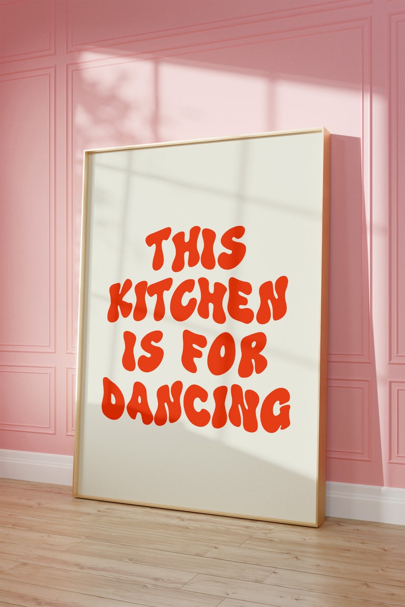 May include: A framed print with the text "This kitchen is for dancing" in red, bubble-like letters on a cream background.