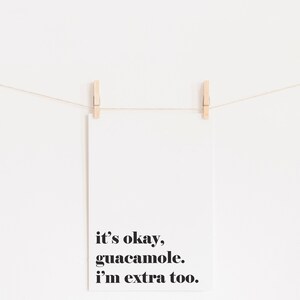 Puede incluir: Una tarjeta blanca con texto negro que dice "it's okay, guacamole. i'm extra too." La tarjeta est&aacute; colgada de una cuerda con dos pinzas de madera.