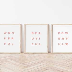 May include: Three framed prints with the words "Wonderful", "Beautiful", and "Powerful" spelled out in a unique way with the letters arranged in a grid pattern. The words are printed in a light pink color on a white background.