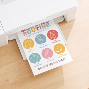 May include: A white printer printing a colorful "Morning Routine" chart. The chart includes illustrated steps like "Wake up," "Brush teeth," and "Eat breakfast." The text "ENJOY YOUR DAY!" is at the bottom.