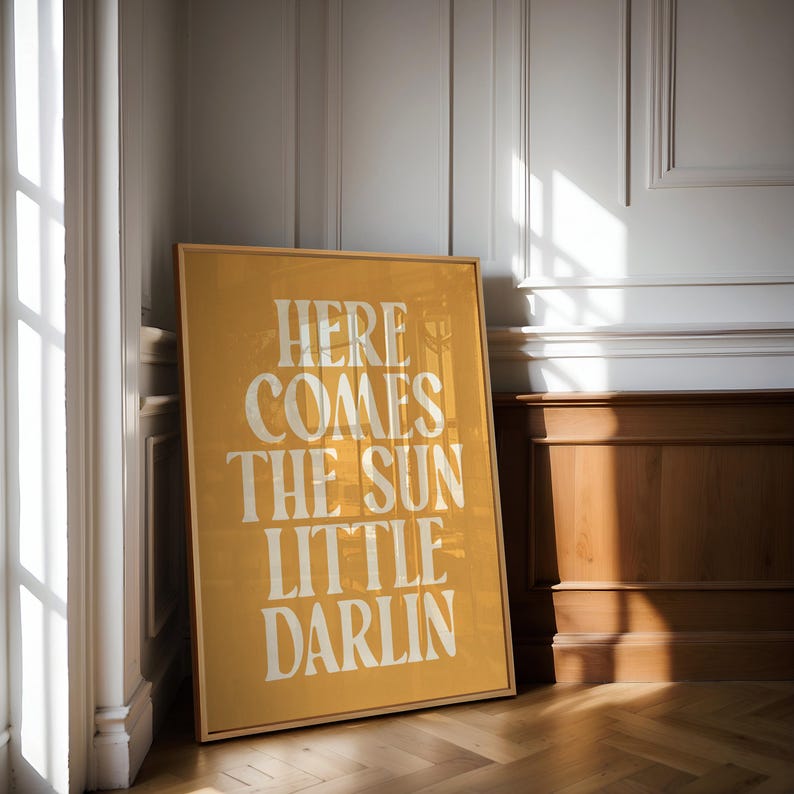 K&ouml;nnte beinhalten: Ein gerahmter Druck mit gelbem Hintergrund und wei&szlig;em Text, der "Here comes the sun little darlin" lautet.