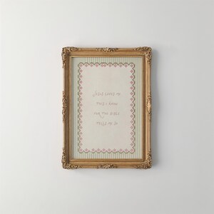 May include: A rectangular gold ornate frame containing a cross-stitch sampler on a light striped background. The embroidery features a pink and green floral border surrounding the text: Jesus loves me this I know for the bible tells me so.