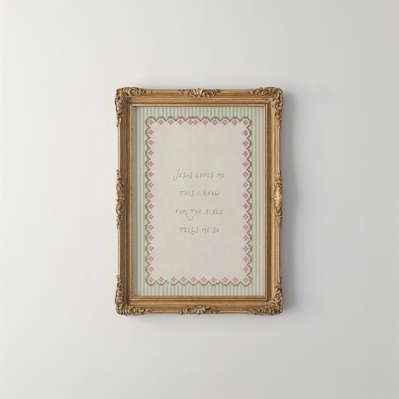 May include: A rectangular gold ornate frame containing a cross-stitch sampler on a light striped background. The embroidery features a pink and green floral border surrounding the text: Jesus loves me this I know for the bible tells me so.