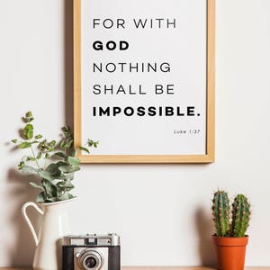 Puede incluir: Una impresi&oacute;n enmarcada con fondo blanco y texto negro que dice "Porque para Dios nada es imposible. Lucas 1:37". La impresi&oacute;n est&aacute; colgada en una pared blanca sobre una mesa de madera con una jarra blanca, una c&aacute;mara vintage y un cactus en maceta.