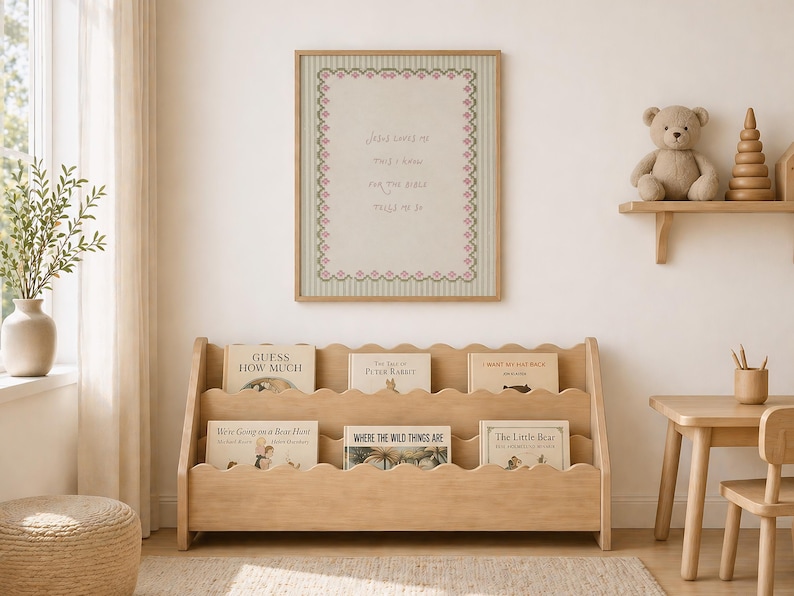 May include: A light wood bookshelf with three scalloped tiers holding children's books. Above it hangs a framed print with a light green striped background, a pink decorative border, and the text: Jesus loves me this I know for the Bible tells me so.