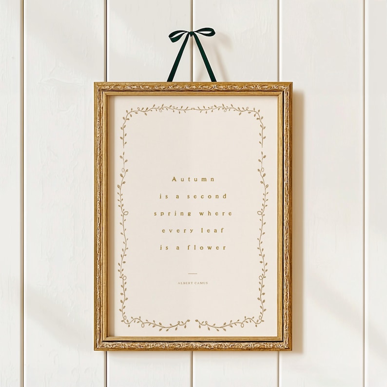 May include: A framed print with a gold-colored ornate frame and a green ribbon for hanging. The print features the quote "Autumn is a second spring where every leaf is a flower" in gold lettering, surrounded by a delicate floral border.