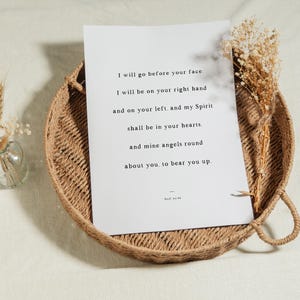 K&ouml;nnte beinhalten: Ein wei&szlig;er Druck mit inspirierendem Text liegt in einem runden Weidenkorb. Der Druck zeigt ein Zitat in schwarzem Text. Getrocknete Blumen und eine kleine Glasvase mit Weizen&auml;hren befinden sich auf der linken Seite des Korbs.