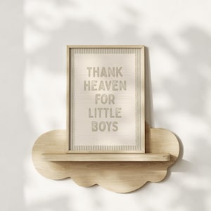 Puede incluir: Un cuadro enmarcado con el texto "THANK HEAVEN FOR LITTLE BOYS" en gris claro. El cuadro se muestra en una estanter&iacute;a de madera con forma de nube, montada en una pared blanca. El marco es de color marr&oacute;n claro.