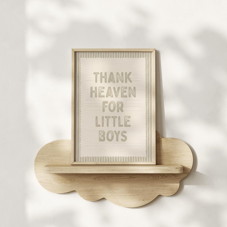 Puede incluir: Un cuadro enmarcado con el texto "THANK HEAVEN FOR LITTLE BOYS" en gris claro. El cuadro se muestra en una estanter&iacute;a de madera con forma de nube, montada en una pared blanca. El marco es de color marr&oacute;n claro.
