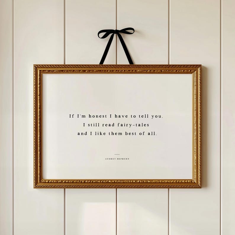 May include: A framed print with a gold ornate border and a black ribbon for hanging. The print features a quote: "If I'm honest I have to tell you. I still read fairy-tales and I like them best of all." The quote is attributed to Audrey Hepburn.