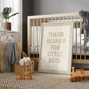 Puede incluir: Una escena de guarder&iacute;a con una cuna de madera, un cuadro enmarcado con la frase "Thank Heaven For Little Boys" y un tren de juguete de madera. Tambi&eacute;n se ven una cesta tejida y una alfombra con un dise&ntilde;o geom&eacute;trico. Peluches y una planta en maceta completan la decoraci&oacute;n.