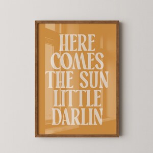 K&ouml;nnte beinhalten: Ein gerahmter Druck mit gelbem Hintergrund und wei&szlig;em Text, der "Here comes the sun little darlin" lautet.