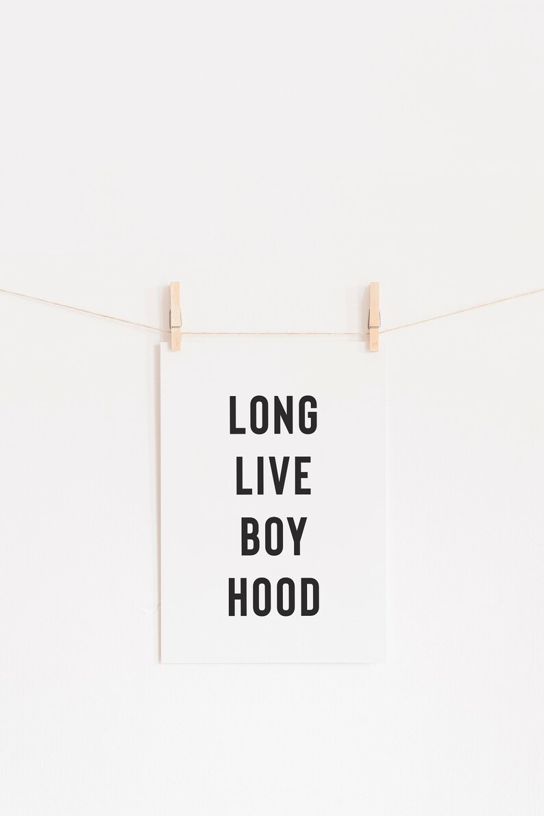May include: A white poster with black text that reads "LONG LIVE BOY HOOD" hanging on a white wall with two wooden clothespins.