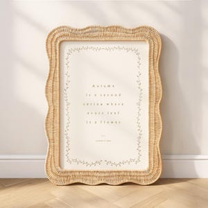 May include: Rectangular framed print with a woven, wavy edge. The print features the quote "Autumn is a second spring where every leaf is a flower" by Albert Camus, surrounded by a floral border. The frame is a light beige color.