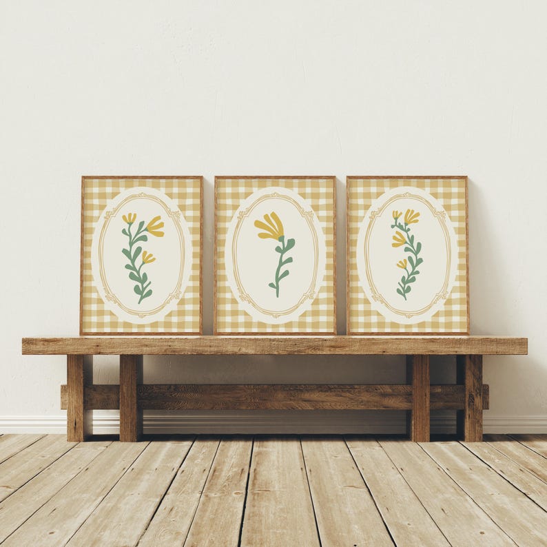 May include: Three framed prints featuring a yellow floral design on a white background with a gingham pattern border. The frames are brown wood.